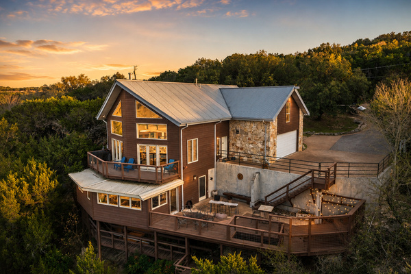 Private Lake Travis retreat surrounded by Hill Country scenery, featuring expansive multi-level decks, multiple outdoor gathering spaces, and beautiful sunset views.