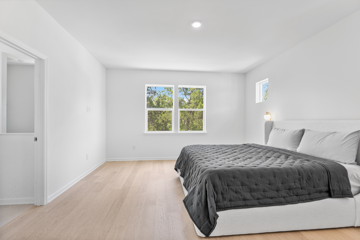 The primary suite waits at the top of the stairs: soft light, treetops framed in the window, and a bed you will be reluctant to leave. Close the door on a full day, breathe out, and let the old oaks rock you to sleep.
