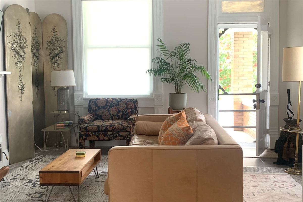 Front door entry fills this living area with natural light - bright, inviting and curated with comfortable seating and vintage charm. 