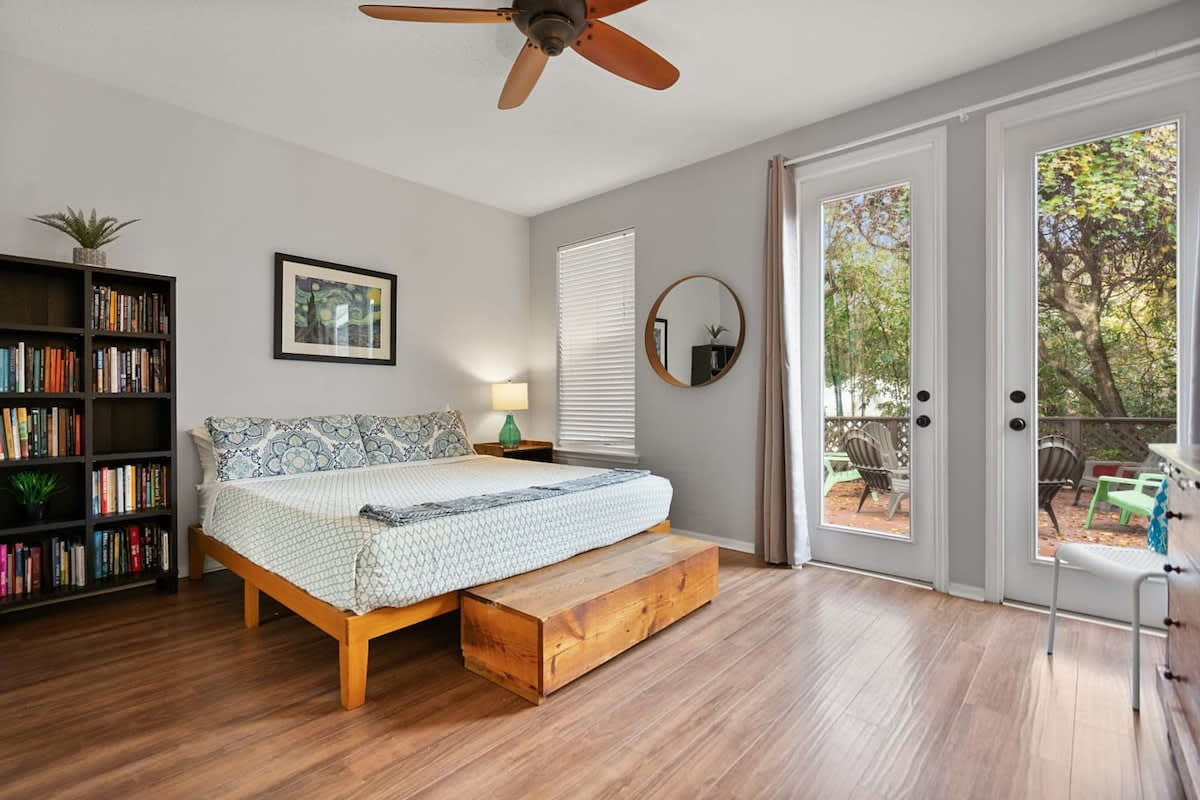 A bedroom that opens onto the garden through its own French doors, with a bookshelf beside the bed. Quiet, green and a little apart from the busier end of the house, for whoever wants the calmest room.