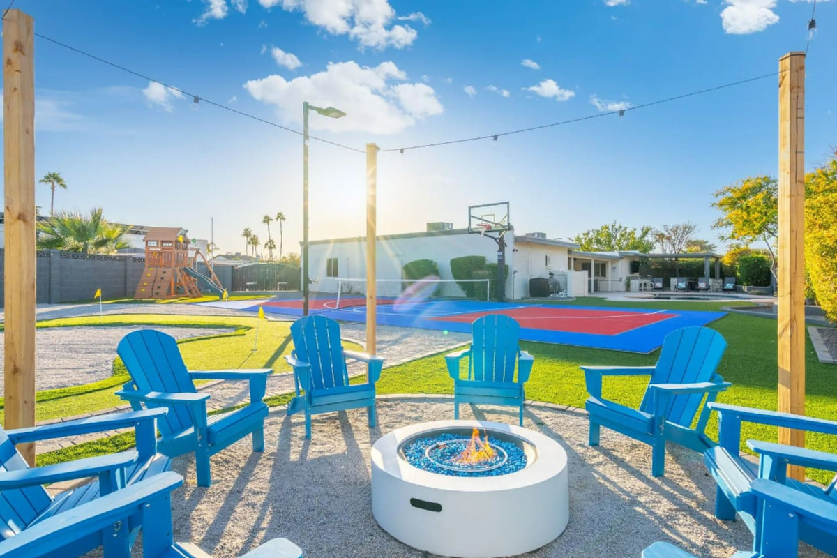 Blue Adirondack chairs ring the fire pit with a full view of the sport court and play structure just beyond, everything the family needs in one glance.