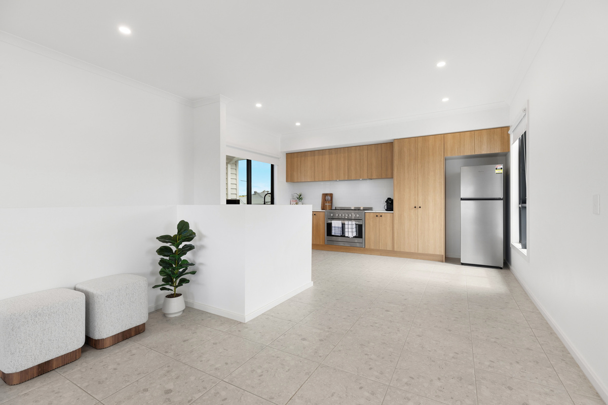 Open-plan kitchen with an island bench, fridge/freezer and timber cabinetry, flowing through to the dining and living areas.