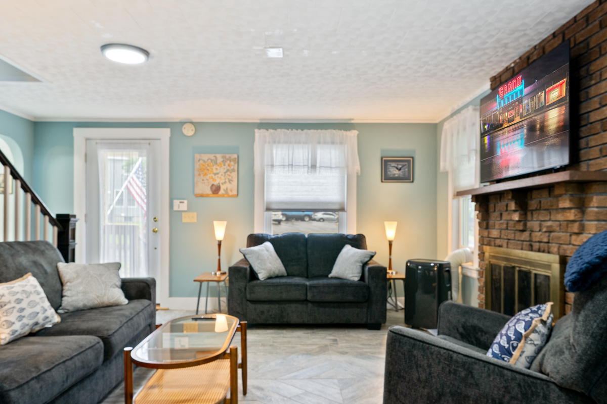 Settle into the comfortable sofa, loveseat, or armchair for a relaxing movie night. This inviting living room features a wide flat-screen TV mounted on a classic brick fireplace, creating the perfect central hub for your group to relax together.