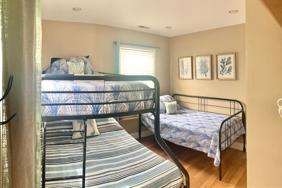 This bright bedroom features a sturdy metal bunk bed and a separate twin bed with coastal-themed linens. The well-appointed area includes charming coral artwork, making it easy to enjoy a restful night before heading to the beach.