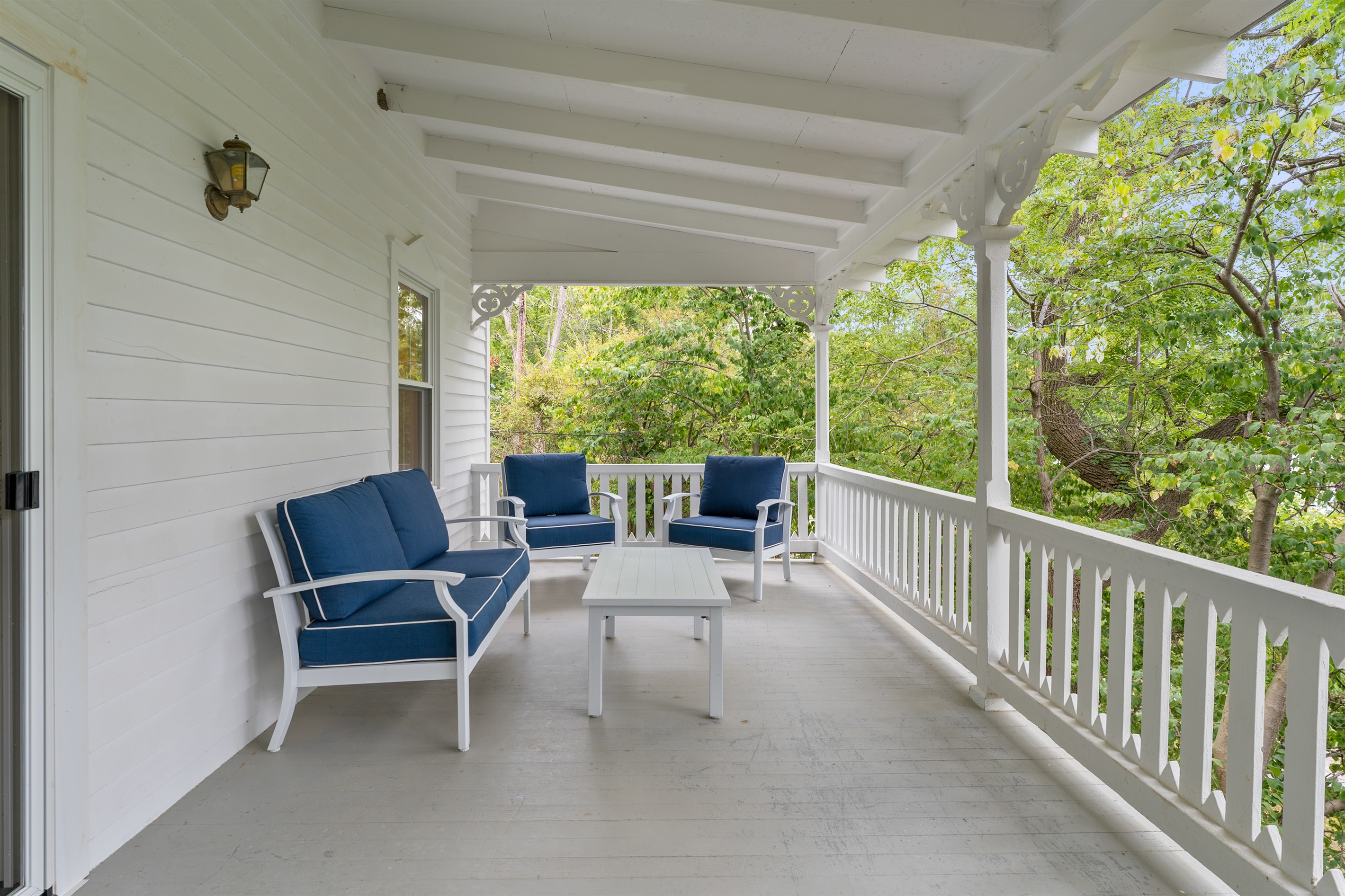 Charming covered porch surrounded by trees, perfect for relaxing with morning coffee or outdoor dining.