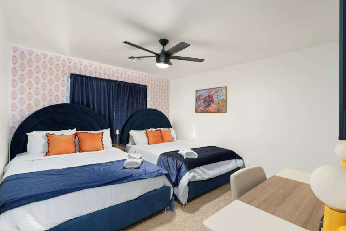 Guest bedroom with bold navy headboards, pink wallpaper accent, and orange pillows—a playful, modern space with personality.