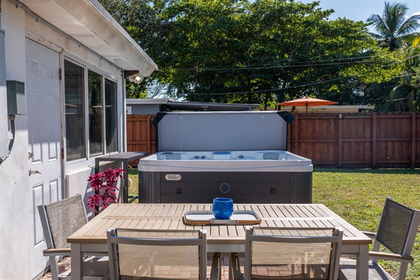 Private fenced backyard with outdoor dining table placed beside the hot tub on the patio