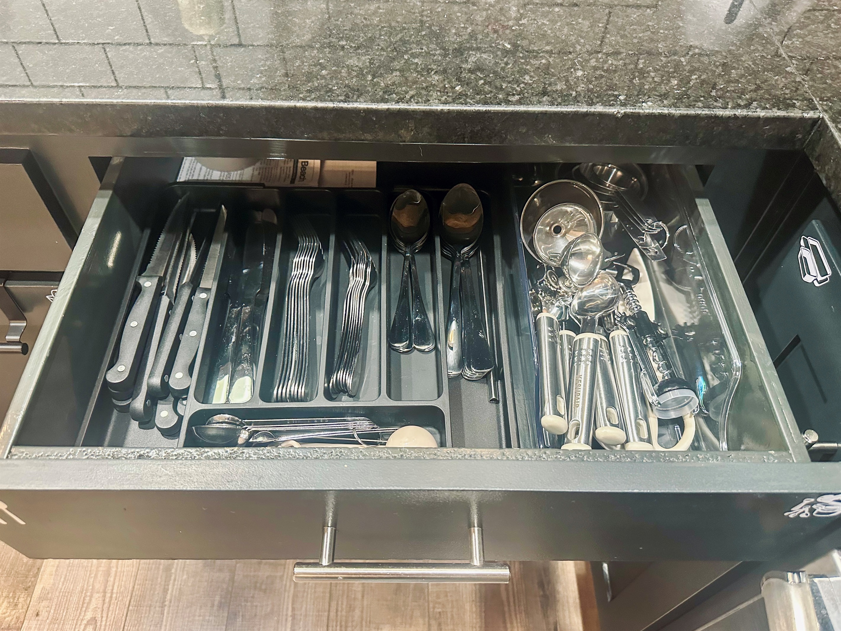 Kitchen drawer stocked with silverware, measuring cups and spoons, and essential cooking utensils for everyday convenience.