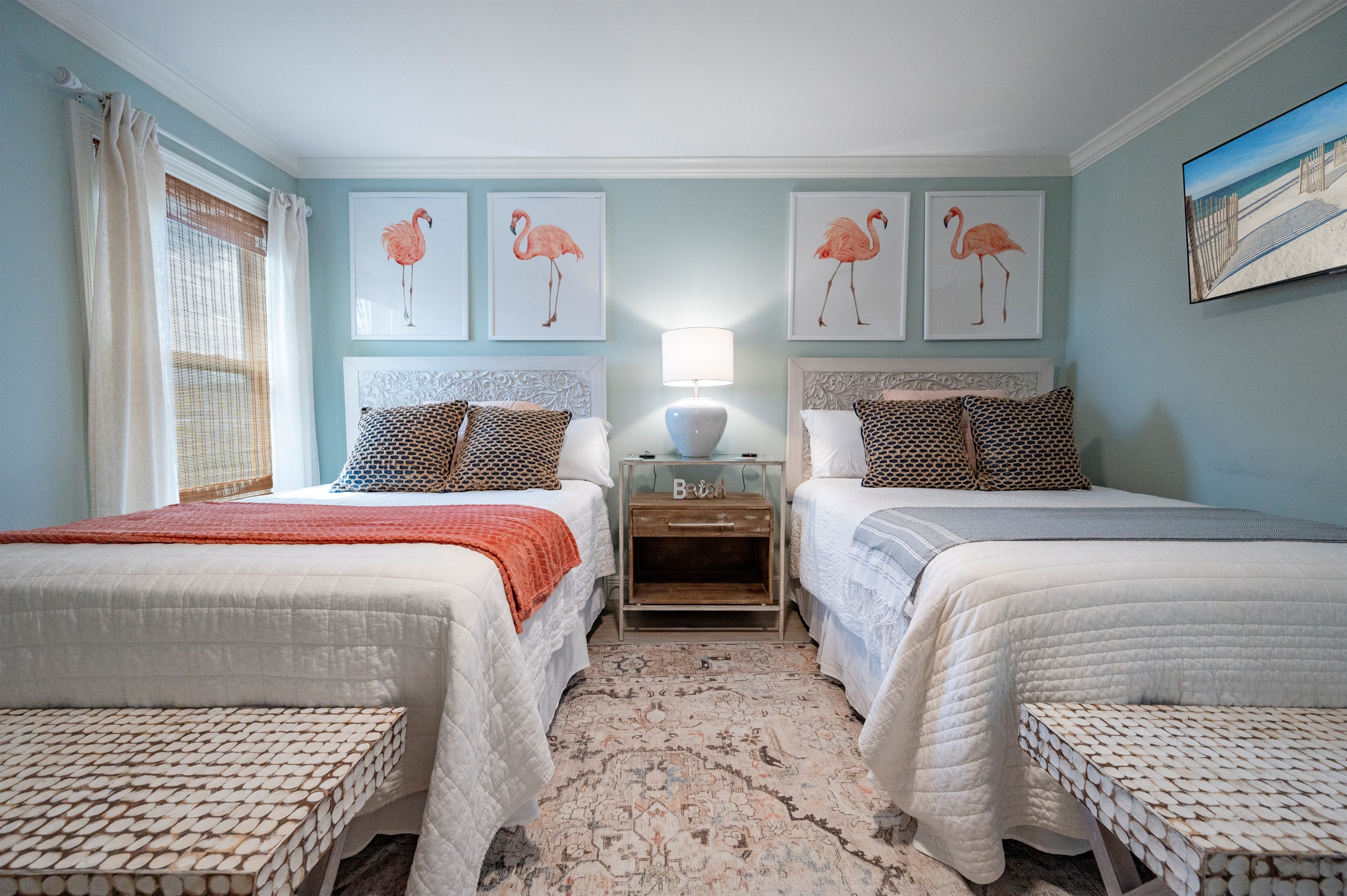 Cozy twin bedroom with flamingo art, soft lighting, beach decor, and charming vibes.
