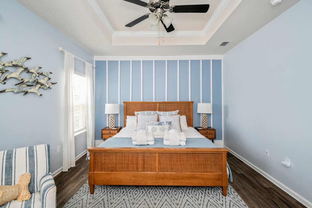 Primary Suite: Elegant King bedroom featuring an en suite bathroom, plush linens, ceiling fan, elegant bedside lamps, dresser, couch, and Smart TV.