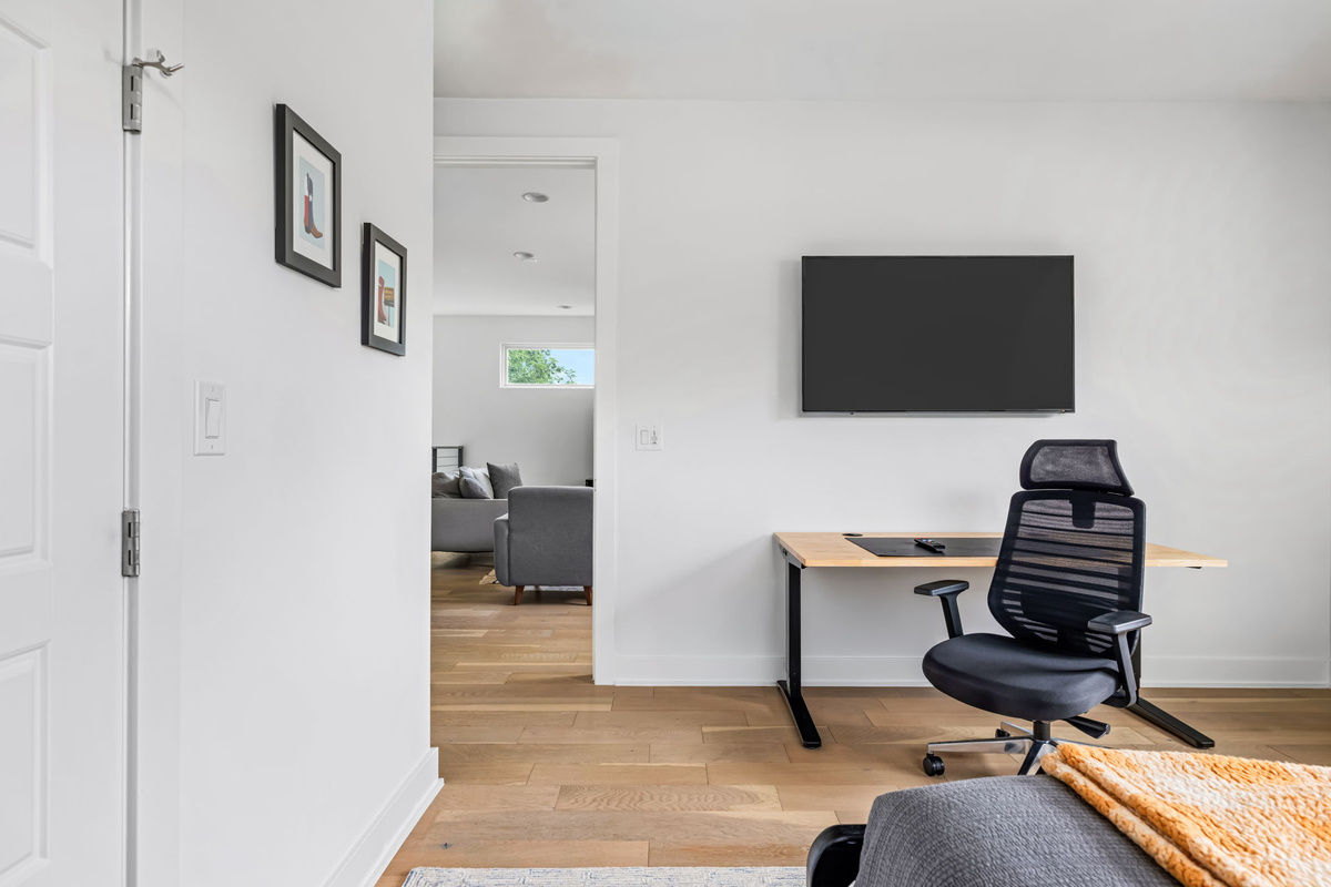 Dedicated workspace featuring a wall-mounted TV/monitor, ergonomic office chair, and sleek desk — perfect for remote work or catching up on emails during your stay.