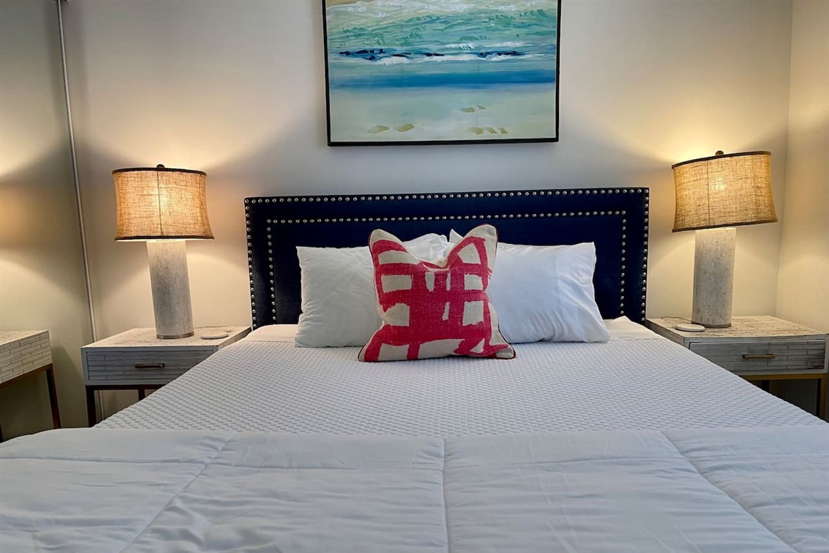 Relax in a queen bed with luxe linens, coastal art, soft lighting, and stylish modern decor.