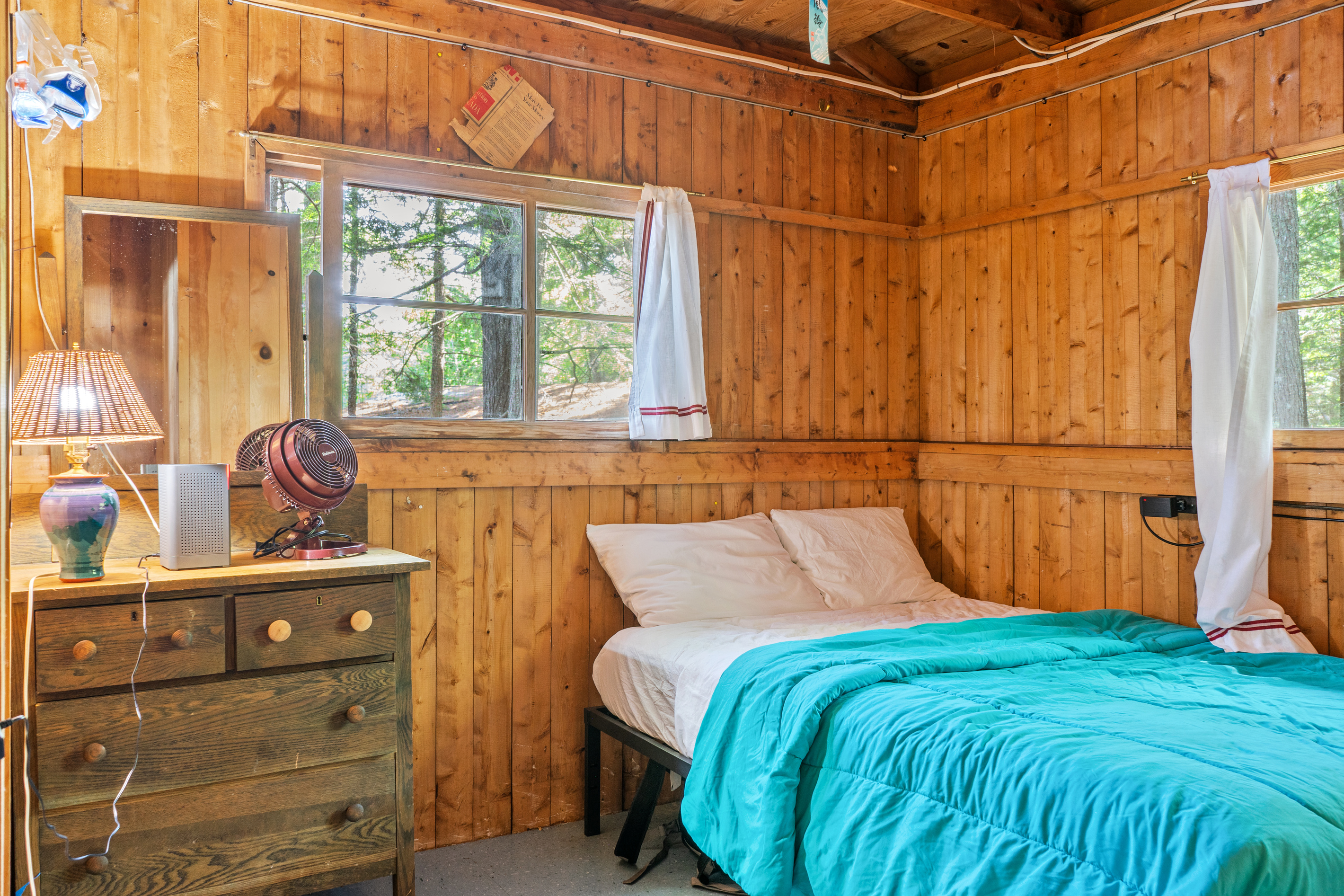 Private guest bedroom at Loonrise Point! Features a full-size bed, full floor-to-ceiling walls for added privacy, wooden dresser with mirror, personal fan, and natural woods views on Beech Hill Pond in Otis, ME.
