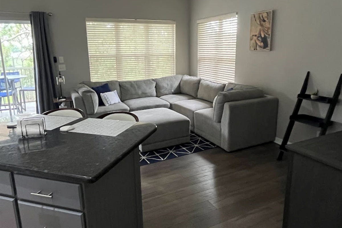 Spacious living area with comfortable sectional seating, wood-look flooring, and large windows for a bright, relaxing feel.