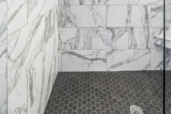 Frameless glass doors reveal stunning marble tile with soft gray veining throughout - Built in niche for convenience and multiple spray heads for a refreshing experience - Soft lighting and stone style flooring create a calming, upscale shower retreat