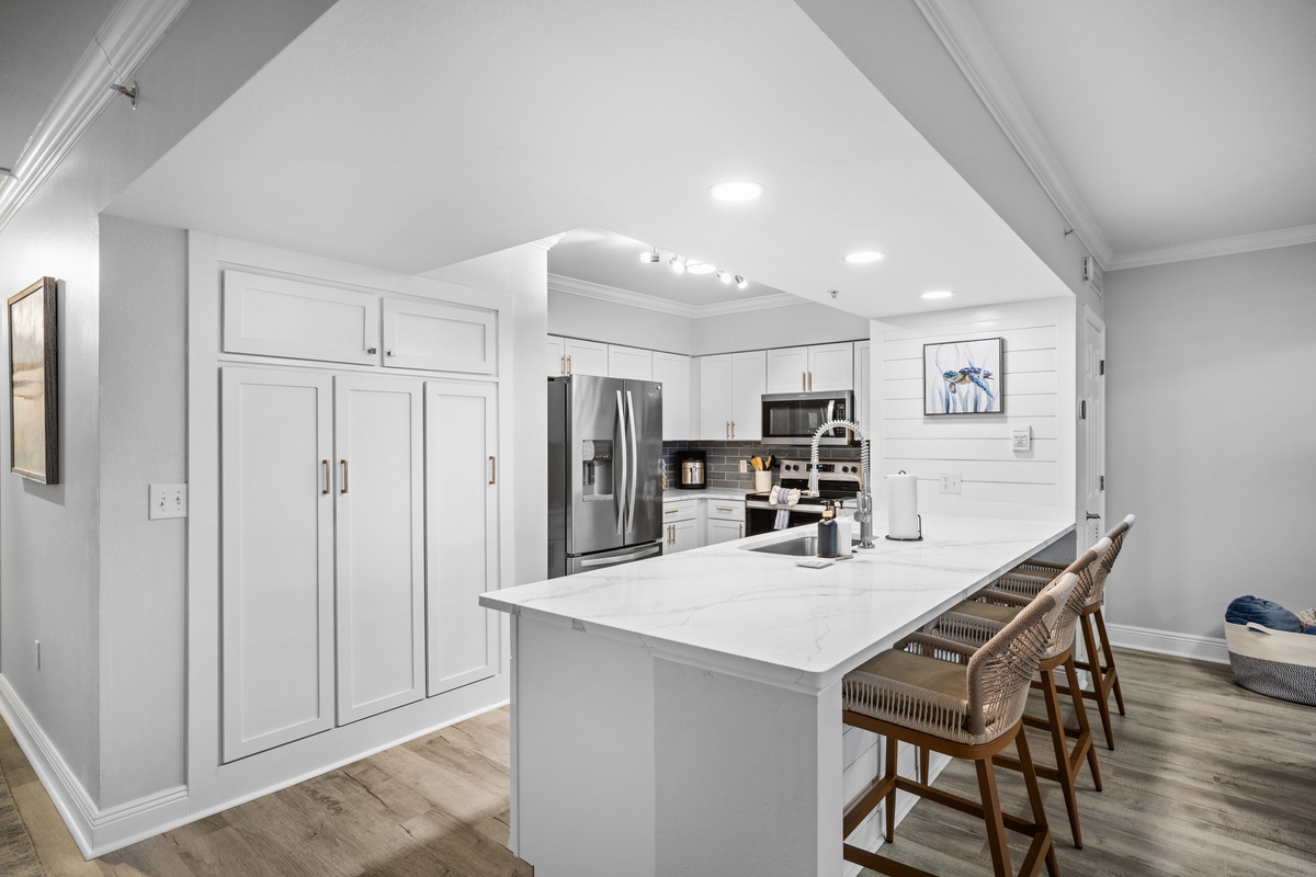 Cook, gather, and unwind in this bright coastal kitchen featuring quartz counters, stainless steel appliances, and bar seating, perfect for meals and conversation after a day at Panama City Beach. 🌊🍽️