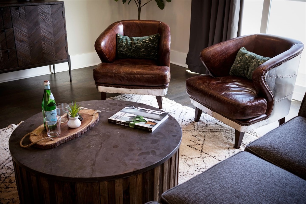 - Rich leather club chairs paired with a rustic wood coffee table create an inviting nook - Decorative tray with sparkling water & greenery adds a polished, welcoming touch - Layered textures & industrial modern vibes make this a perfect spot to unwind