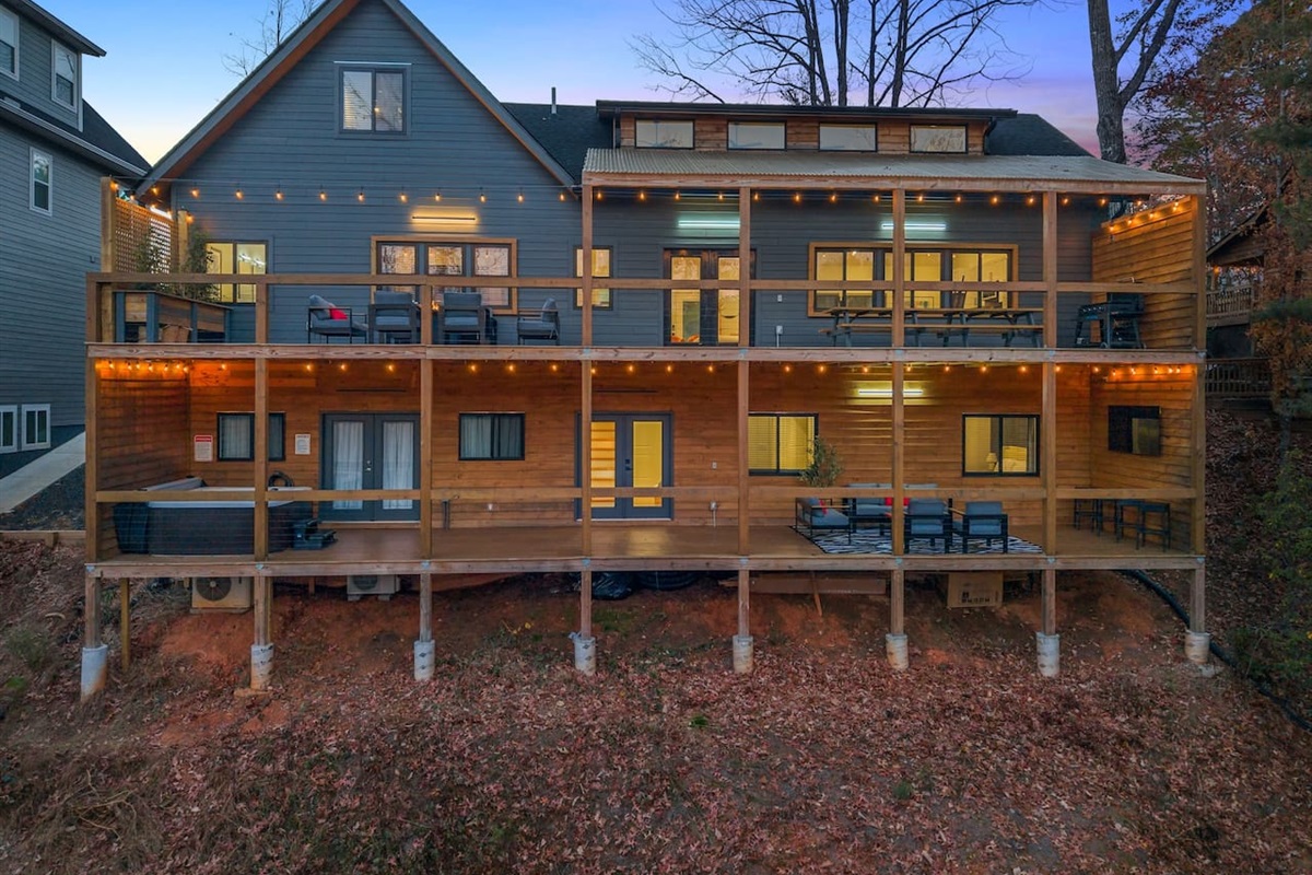 Two-level decks at twilight with a propane fire pit, outdoor TV, and hot tub—perfect for cozy evenings under the lights
