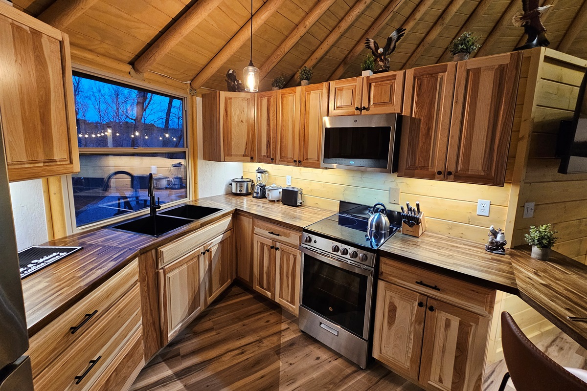 Warm, fully equipped kitchen at Eagle Retreat featuring custom wood cabinetry, full-size stove and oven, microwave, dishwasher, and modern farmhouse sink—perfect for cooking meals after a day