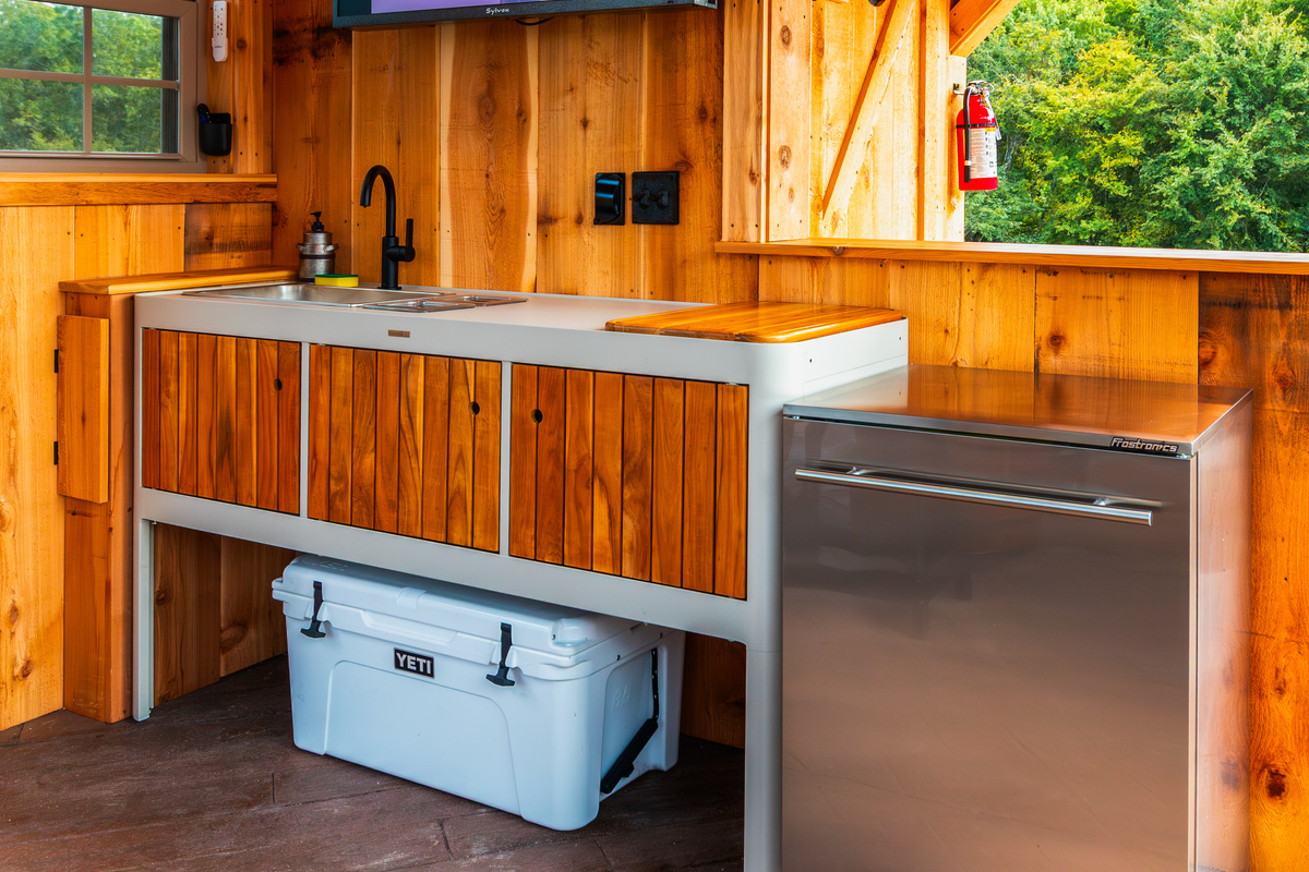 Outdoor kitchen setup with sink, beverage refrigerator, cooler space, and covered prep area.