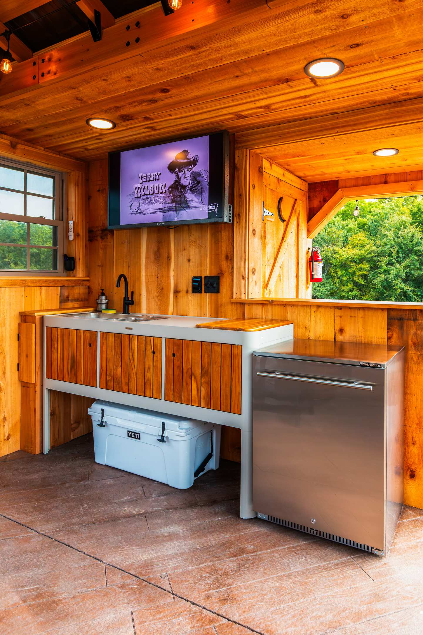 Outdoor kitchen setup with sink, beverage refrigerator, cooler space, and covered prep area.