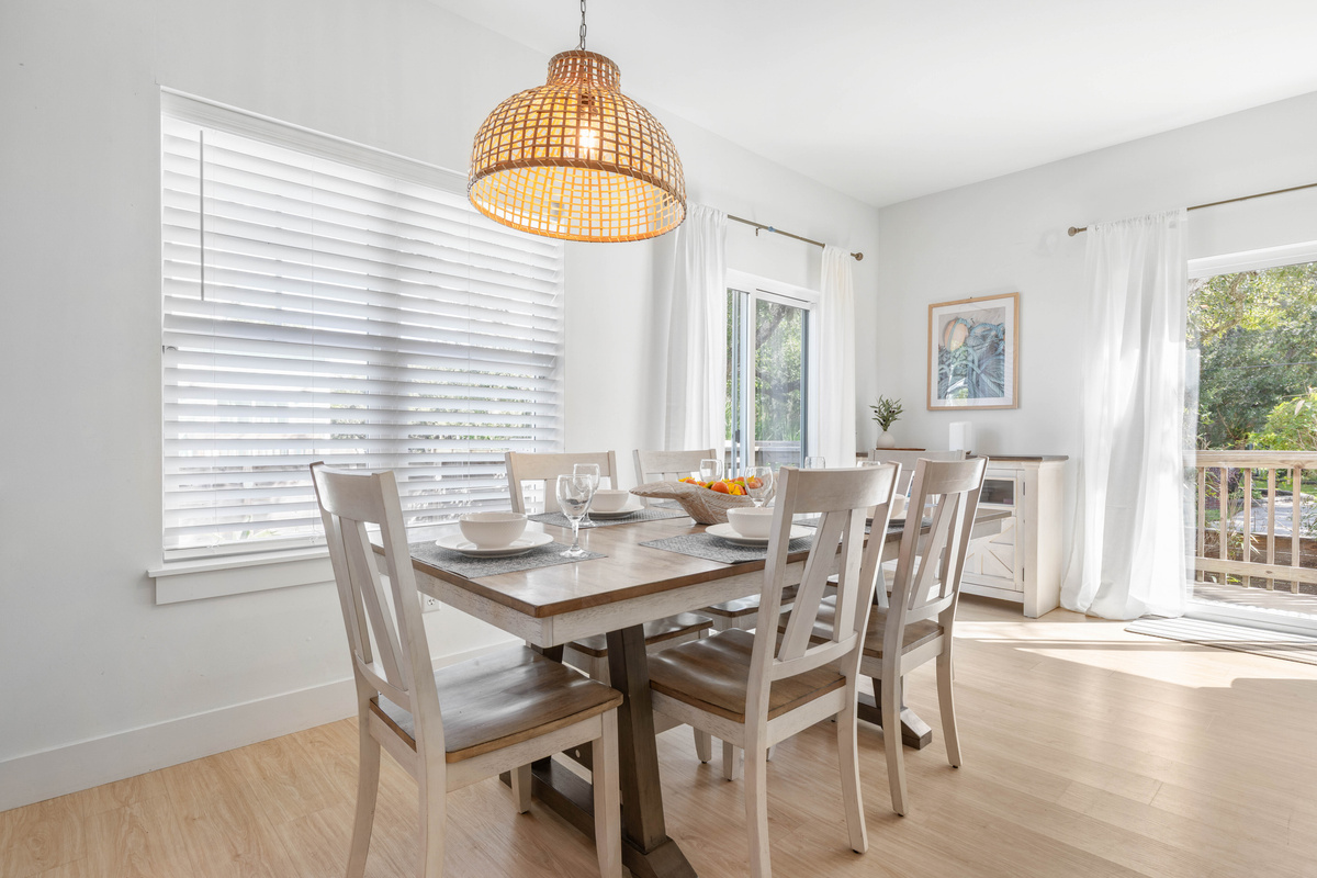 Six chairs beneath a woven pendant, with shutters that soften the afternoon light. Board games take over this table between meals, and the sideboard behind it keeps the puzzle boxes and the decent corkscrew.