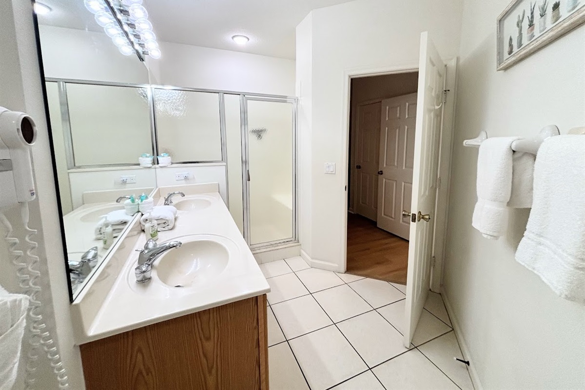 Bright bathroom featuring a large vanity, tile flooring, and a clean shower enclosure.