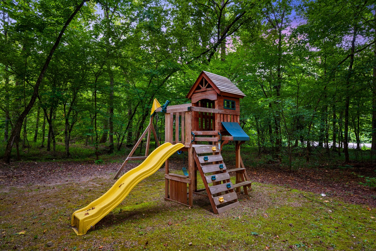 Spacious outdoor playset with slide, swings, climbing wall, and fort — a perfect forest playground for kids to enjoy.