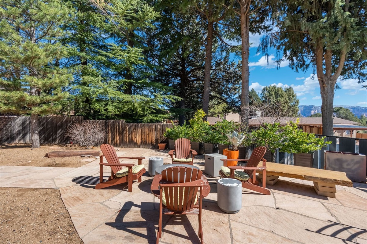 Spacious backyard patio with Adirondack seating and a central fire pit area, surrounded by mature trees and mountain views — a perfect gathering spot to relax and enjoy the fresh air.
