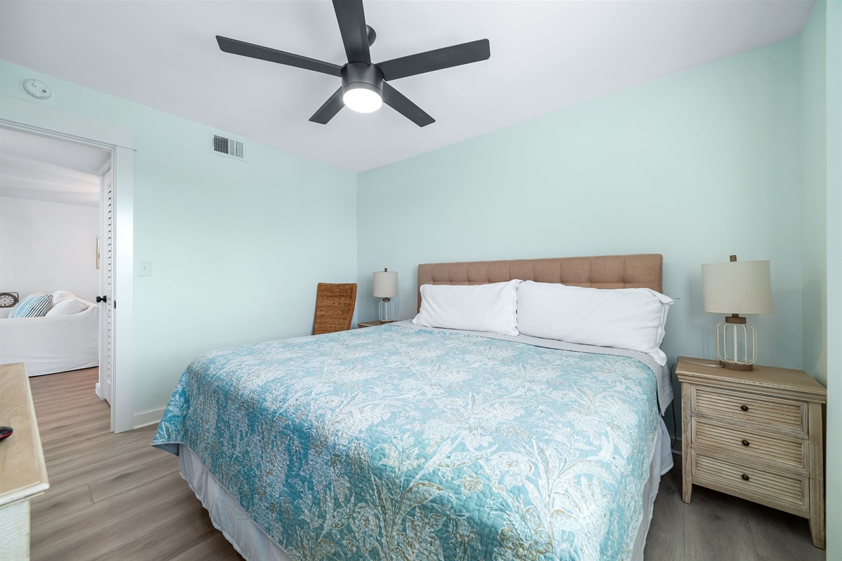 This well-appointed guest room features a king -size bed with a decorative headboard, coastal colored bedding, matching nightstands with lamps, and tile flooring for easy maintenance.