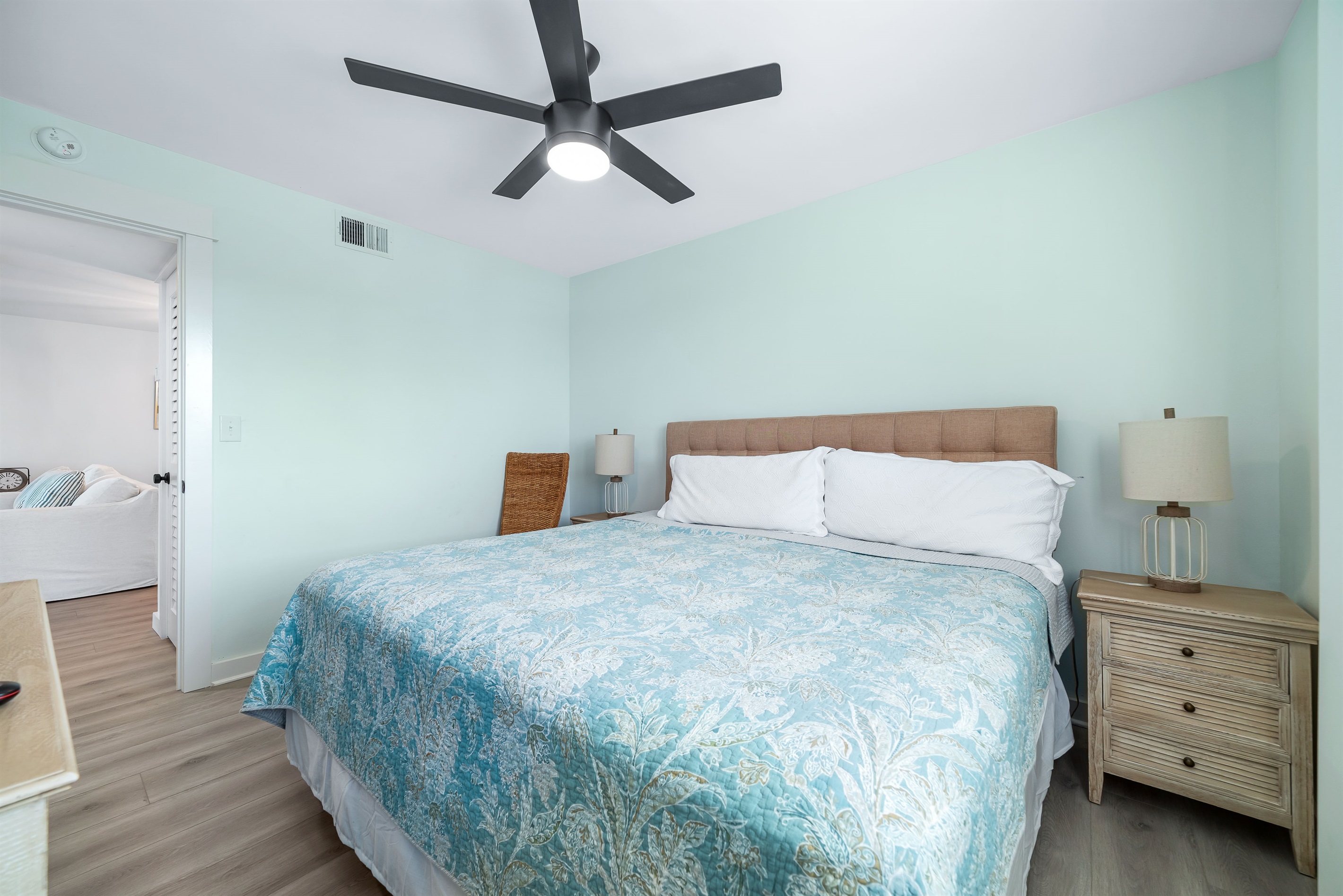 This well-appointed guest room features a king -size bed with a decorative headboard, coastal colored bedding, matching nightstands with lamps, and tile flooring for easy maintenance.