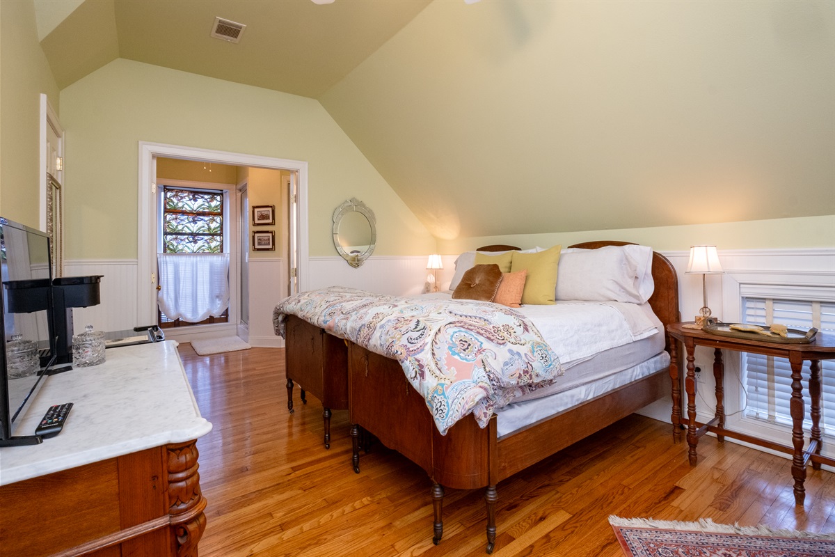 Garden Spa Suite bedroom with a king bed, sloped ceiling, and original hardwood floors.