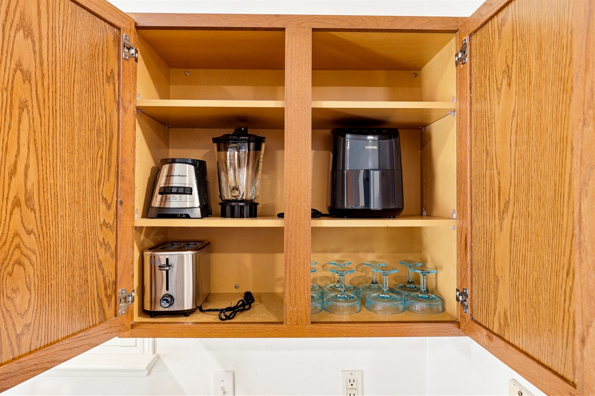 Kitchen cabinet stocked with blender, air fryer, toaster, and wine glasses — bonus appliances that go well beyond the basics for guests who love to cook or entertain.
