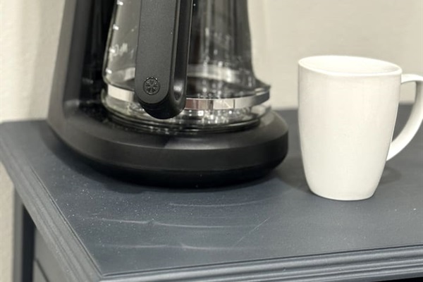 Drop coffee pot maker located on the coffee and wine bar.  Check the freezer for ground coffee.