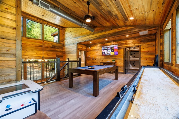 A stunning game room with a pool table, shuffleboard, and wood-accented walls, offering the ultimate entertainment experience. This vacation rental amenity is perfect for families, friends, and corporate retreats.
