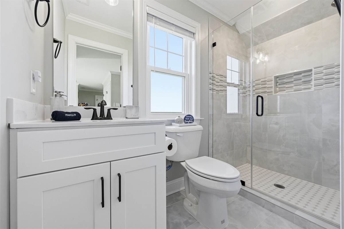 Bright and modern top-level bathroom featuring a custom tiled walk-in shower with stylish coastal-inspired finishes
