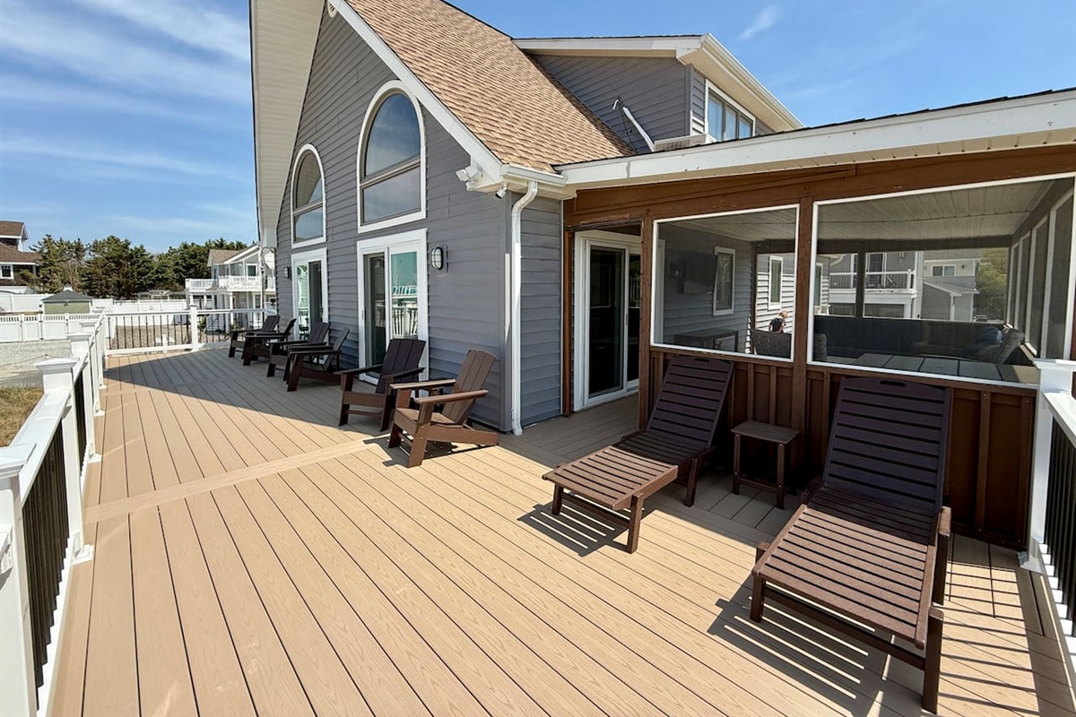 You can see an expansive outdoor deck featuring comfortable seating arrangements, including multiple lounge chairs and Adirondack-style chairs. This inviting space serves as an excellent spot for relaxing outside adjacent to the home.