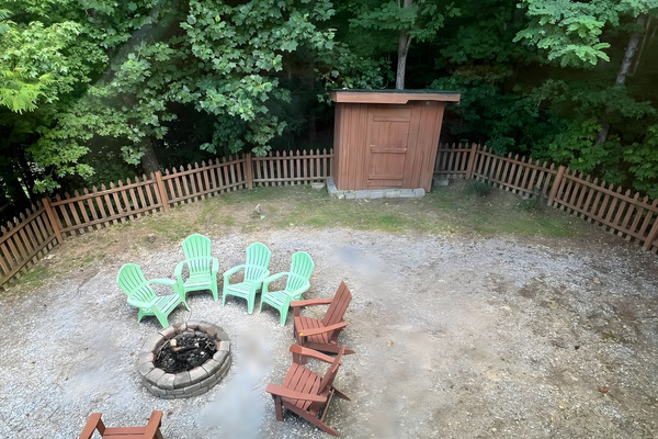 This cozy outdoor setup highlights a wood-burning stone firepit surrounded by plenty of seating, nestled right against a peaceful, wooded backdrop.