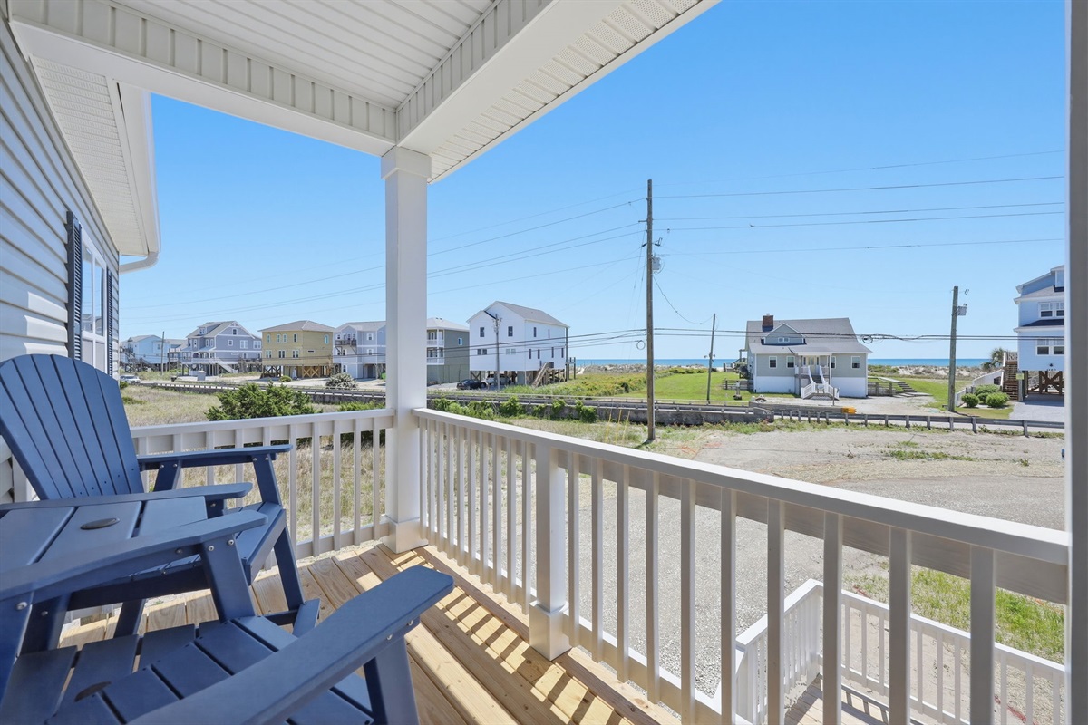 Covered front porch with Adirondack seating and peekaboo ocean views&mdash;perfect for morning coffee or sunset unwinding