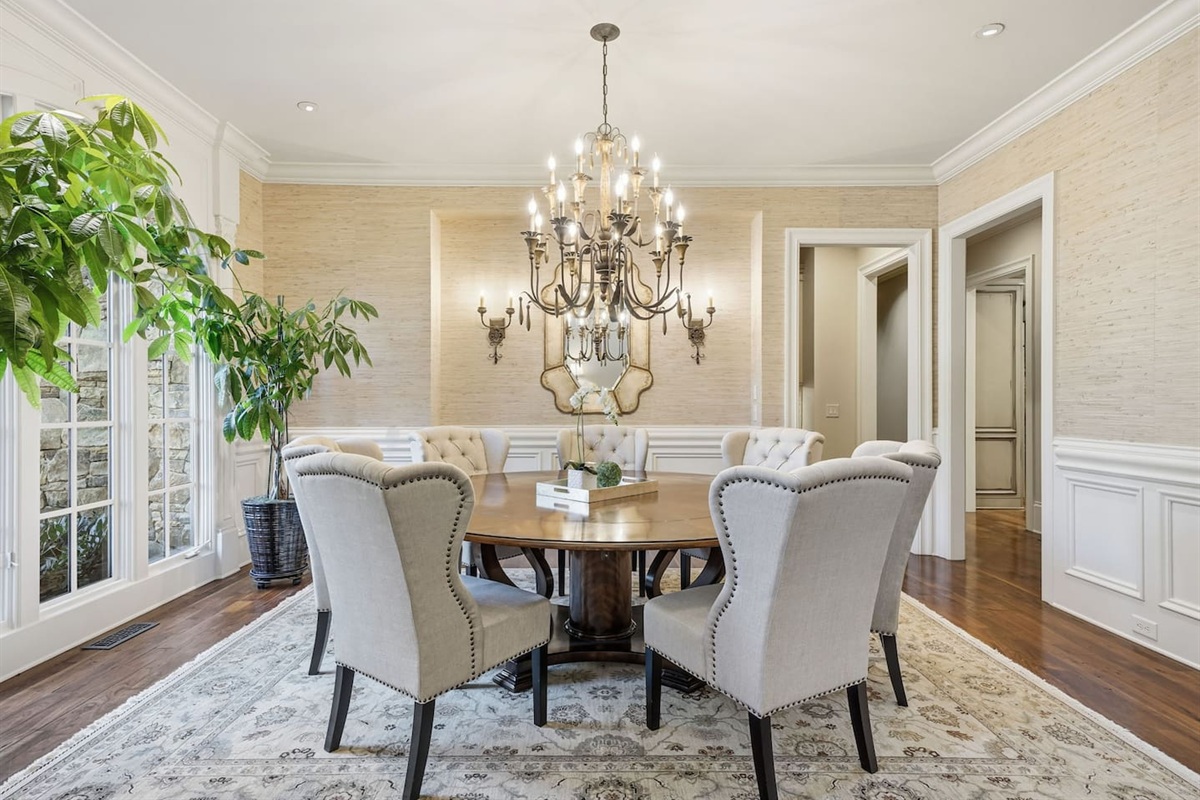 Spacious main dining room to the left of the foyer, featuring a chandelier, seating for seven, and lush green plants. A bright, welcoming space perfect for shared meals or special gatherings.