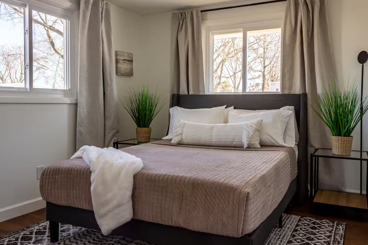 Natural light pours through two windows, framing a bed made for slow mornings.