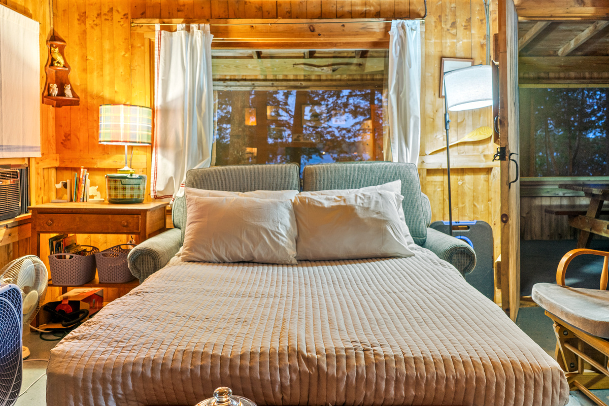 Close-up of converted sleeper sofa at Loonrise Point! Full pull-out bed made up beneath the picture window and window AC unit. Ideal extra sleeping space with lake views in our authentic, uninsulated seasonal camp in Otis, ME