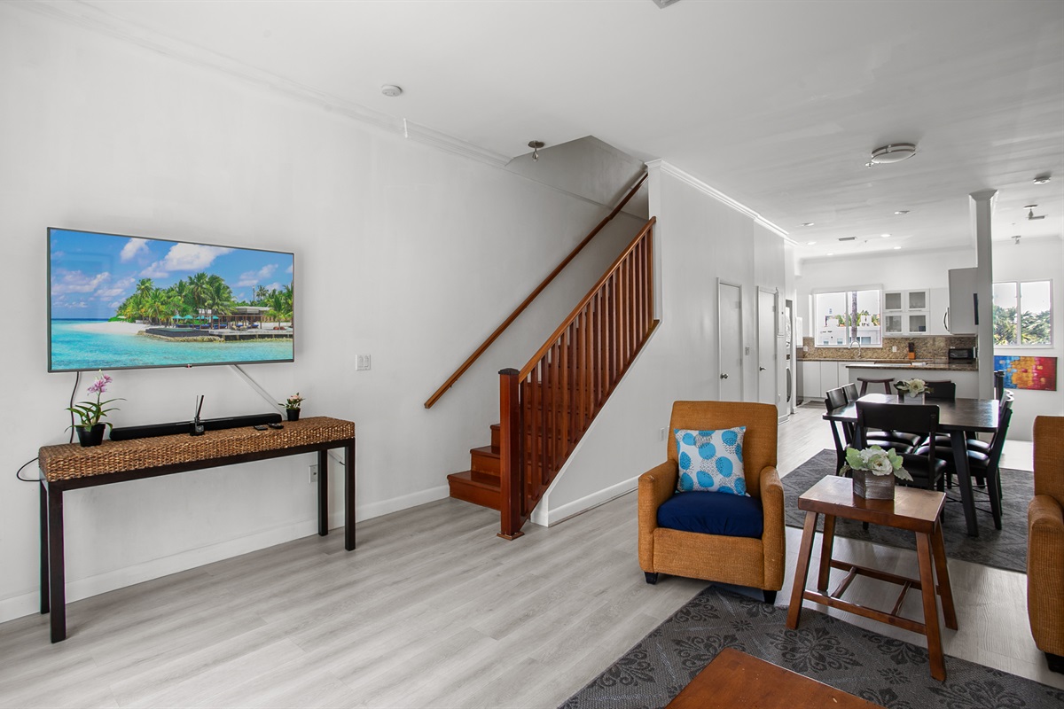 Living room with leather sofa, accent chairs, and a 50-inch flat screen TV. Sliding glass doors open to a Juliet balcony for sea breeze.