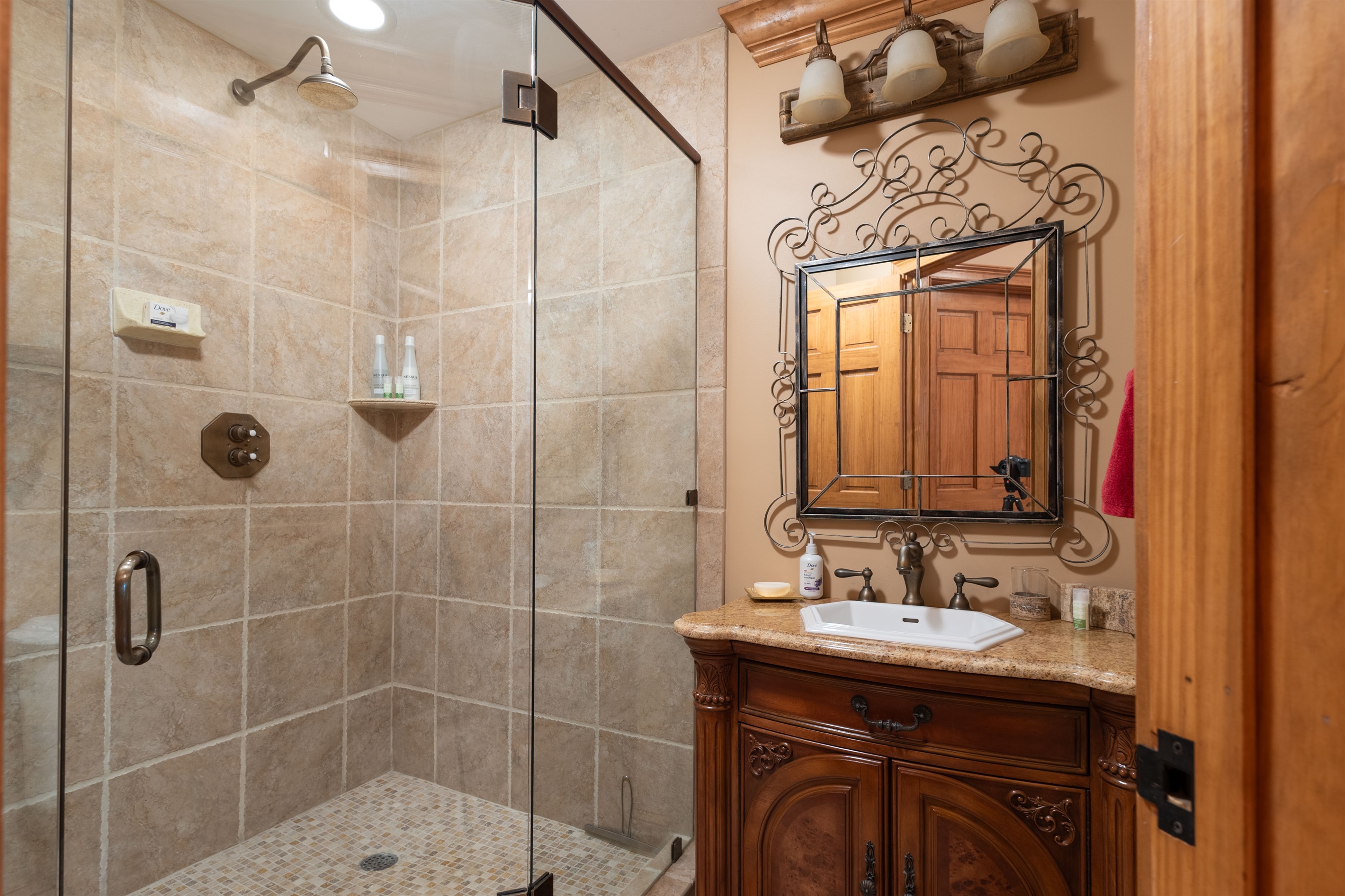 Warm wood cabinetry, detailed iron accents, and a large walk-in shower create a cozy yet upscale bathroom retreat.
