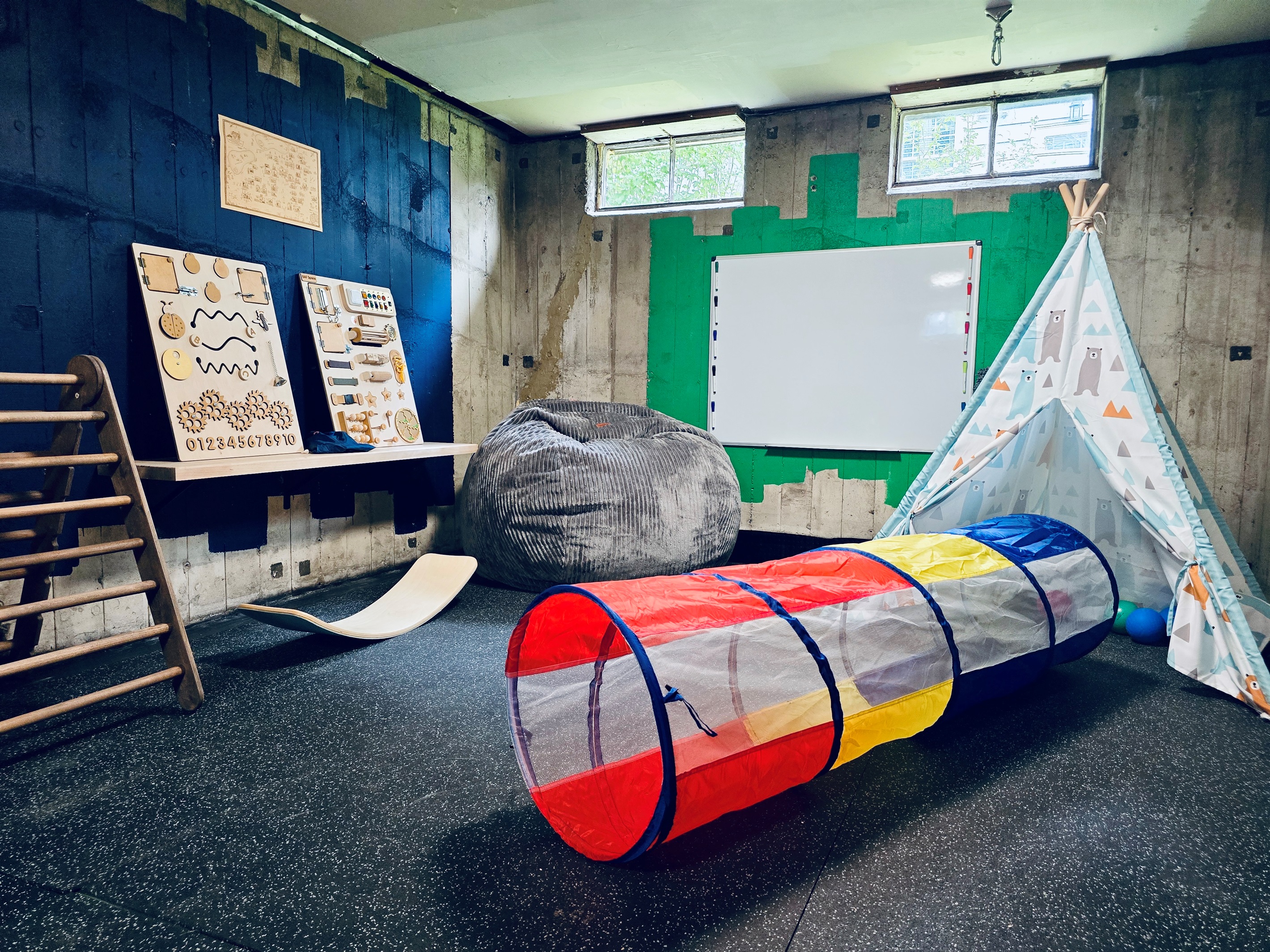 Teepee, climbers, sensory boards, and creative tools fill this industrial-chic play zone. Toys rotate by age, and a ceiling-mounted sensory swing is stored in the bench for added fun.
