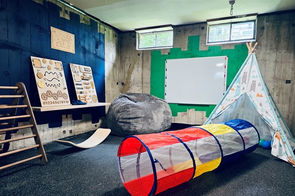 Teepee, climbers, sensory boards, and creative tools fill this industrial-chic play zone. Toys rotate by age, and a ceiling-mounted sensory swing is stored in the bench for added fun.