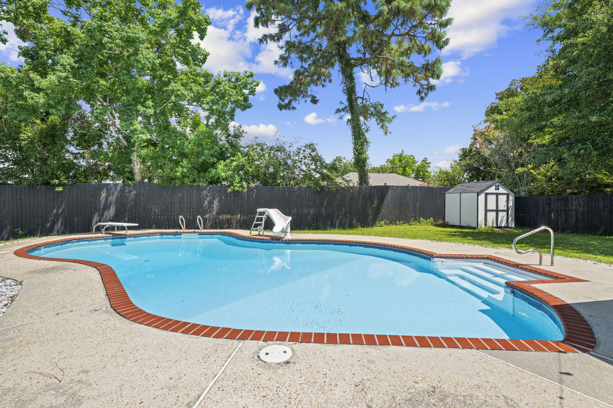 Plenty of sunny deck space to lounge poolside, with a storage shed and lush green backdrop.