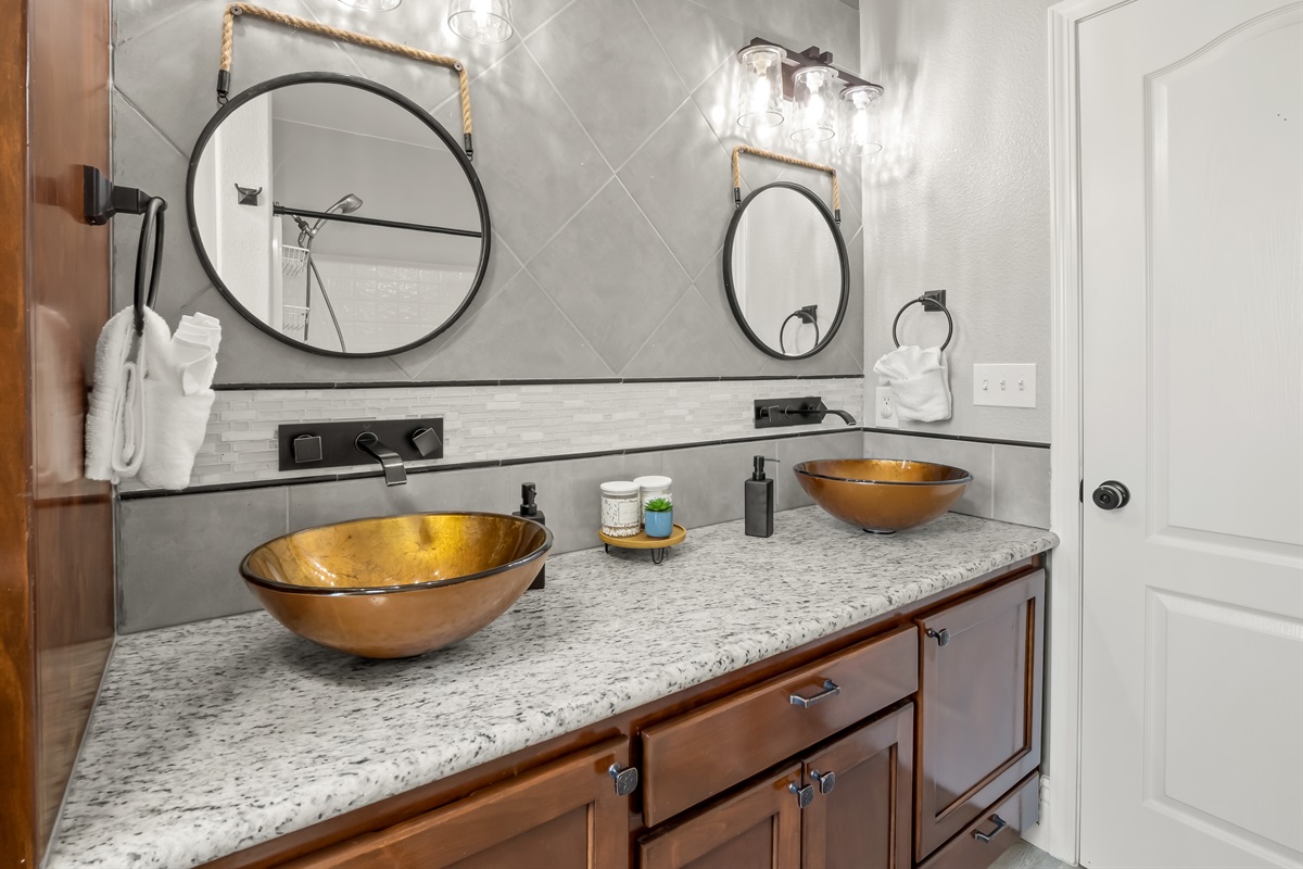 Striking dual vessel sinks, granite countertops, and designer lighting create a spa-inspired retreat with elevated style.