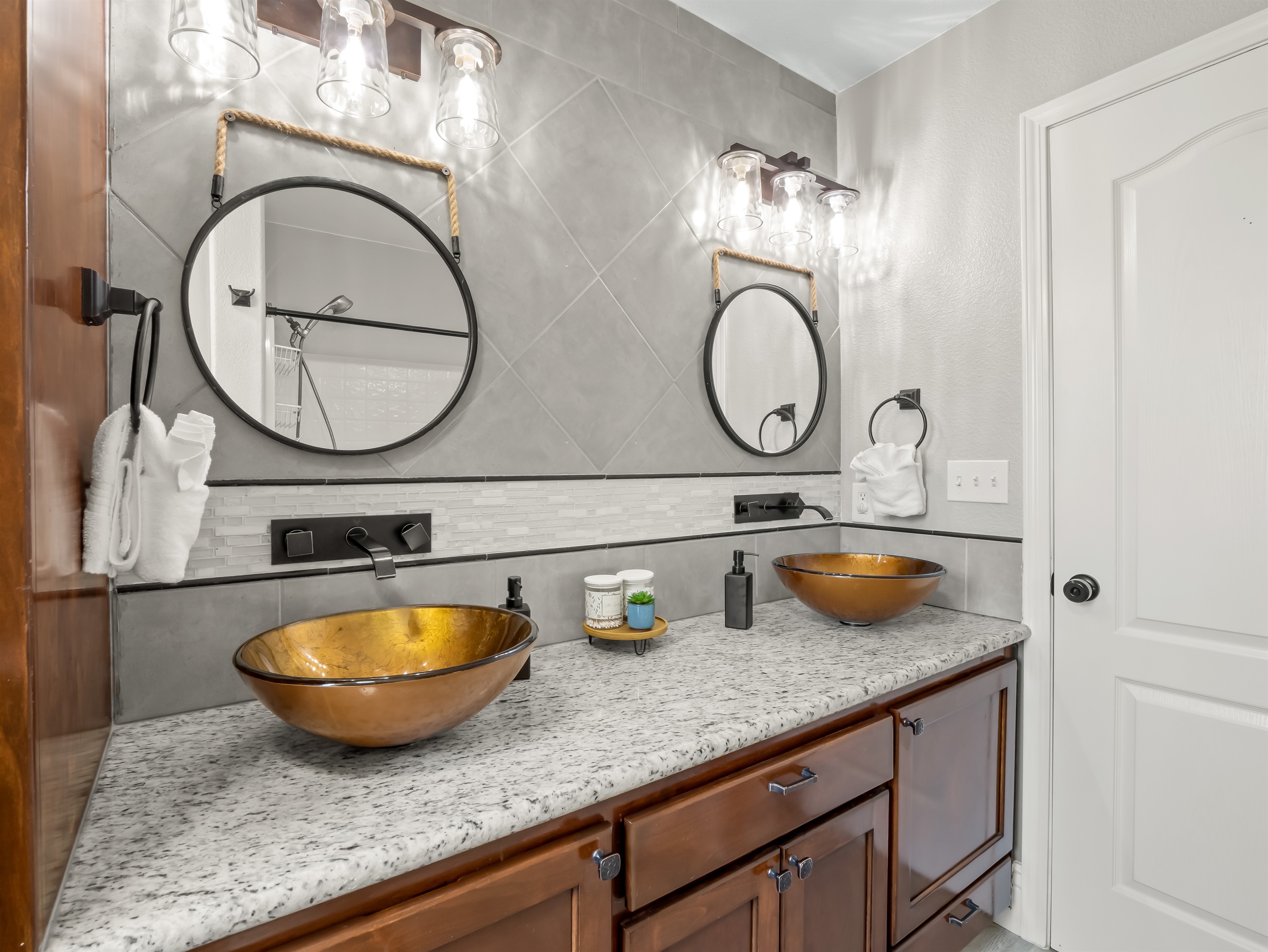 Striking dual vessel sinks, granite countertops, and designer lighting create a spa-inspired retreat with elevated style.