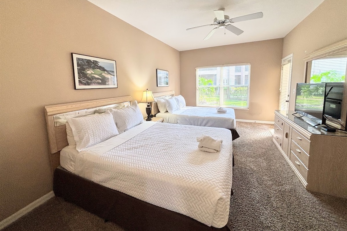 Comfortable bedroom featuring two beds, ceiling fan, TV, dresser storage, and plenty of natural light.